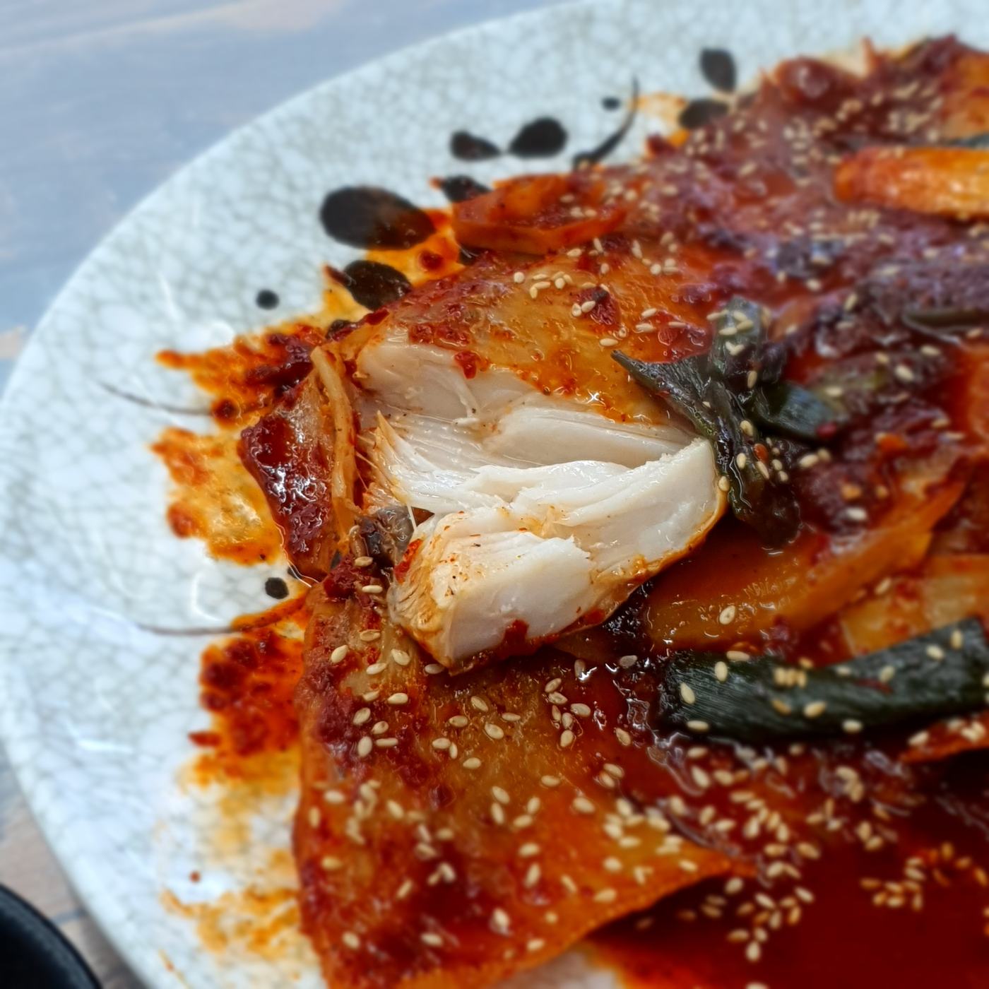 가오리찜의 하얀 속살 클로즈업, 깨와 대파가 올라간 양념