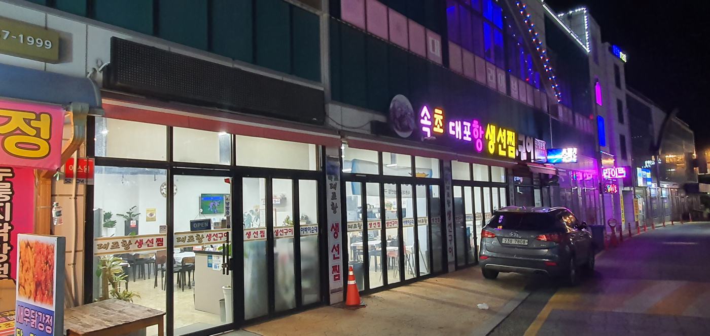 밤에 불이 켜진 속초 대포항 생선찜 구이 간판과 매장 입구